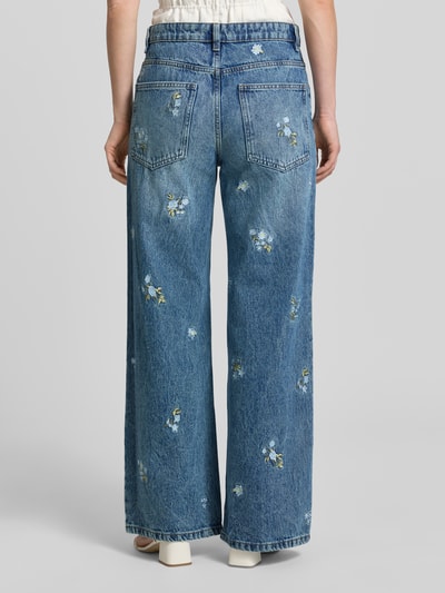 Frauenmodel trägt Wide Fit Jeans mit floralem Allover-Stitching Modell 'BEVERLY' von Mango aus Reine Baumwolle im 5-Pocket-Design, Knopf-Reißverschluss, blauer Denim mit Blumen-Stitchings, Bundweite bei Größe 36: 40 cm, Innenbeinlänge bei Größe 36: 79 cm, Ganzkörperansicht Rückansicht.