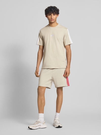 Männermodel trägt Regular Fit Sweatshorts aus Baumwoll-Mix von adidas Sportswear, unifarben, Logo-Stitching, Kontraststreifen, Ganzkörperansicht von vorne.