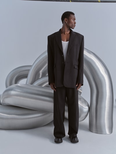 Männermodel trägt Relaxed Fit Sakko aus Woll-Mix von VETEMENTS in Schwarz mit Knopfverschluss, Patten- und Brusttasche, Reverskragen, Ganzkörperansicht von vorne