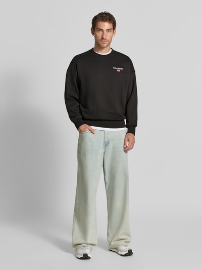 Męski model nosi Relaxed Fit Sweatshirt aus Baumwoll-Mix von Polo Ralph Lauren, czarny kolor, szerokie jeansy, białe sneakersy, gładka tekstura, Ganzkörperansicht von vorne.