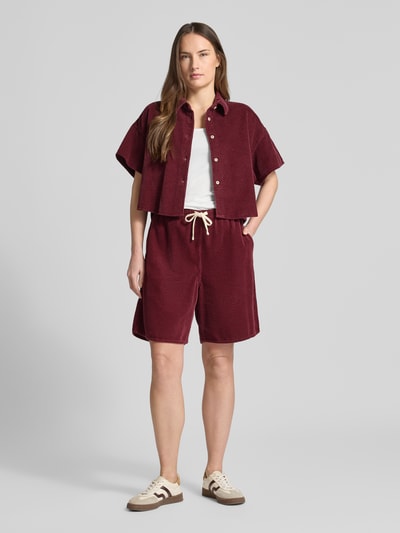 Modelka nosi bordowe Shorts mit elastischem Bund Modell 'PADOW' von American Vintage z czystej wiskozy, luźny krój, kieszeń z tyłu, tunel w pasie, Szerokość w rozmiarze S: 37 cm, długość nogawki wewnętrznej S: 20 cm, widok całej sylwetki z przodu.