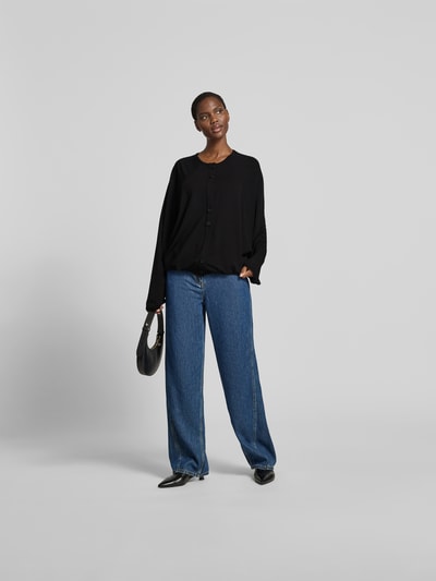 Frauenmodel trägt Oversized Cardigan aus Lyocell-Mix von black palms in Schwarz, mit Rundhalsausschnitt, Knopfleiste, elastische Abschlüsse, Oversized-Fit, kombiniert zu blauer Jeans, Rückenlänge 58 cm bei Größe S/M, Ganzkörperansicht von vorne.