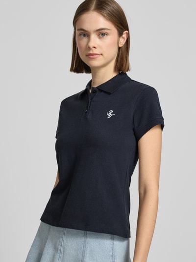 Vrouwenmodel draagt Kurzärmliges Poloshirt in Piquéoptik mit Kragen und Logostickerei van REVIEW in zwart, slim fit, van zuivere katoen, piquéstructuur, polokraag, korte mouwen, logostiksel, ruglengte maat S 52 cm, driekwartvooraanzicht van bovenlichaam