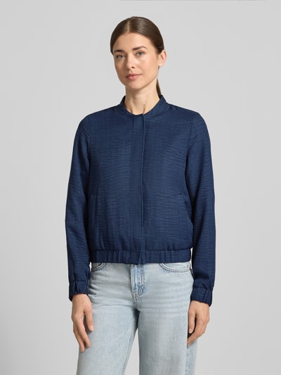 Modelka kobieca nosi Regular Fit Blouson mit Baseball-Kragen Modell 'MELANEY' od Vero Moda, melange, długie rękawy, kieszenie boczne, krój regular fit, widok całego ciała z przodu.