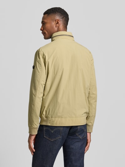 Männermodel trägt Regular Fit Jacke mit Stehkragen von bugatti in Beige mit elastischen Abschlüssen und Logo-Detail, Ganzkörperansicht Rückansicht.