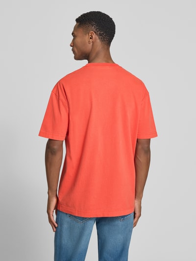 Męski model nosi T-Shirt z label-printem model 'JOEL' od Samsøe Samsøe, bawełna, krój relaxed fit, kolor czerwony, widok całej sylwetki z tyłu.