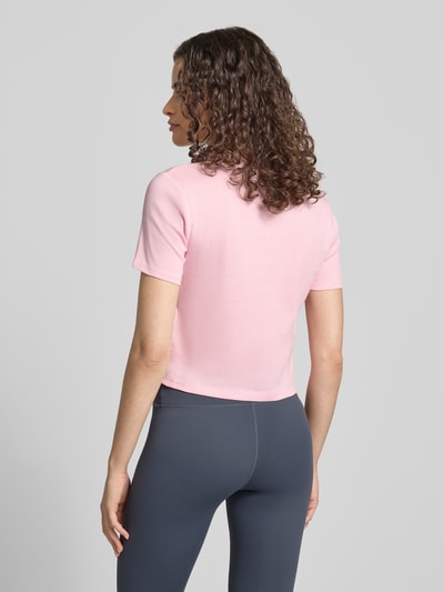 Kobiece model prezentuje t-shirt z okrągłym dekoltem od Topshop z bawełny, taliowany krój, krój krótki, długość tyłu w rozmiarze S: 47 cm, jasnoróżowy kolor, gładka tekstura, widok całej sylwetki z tyłu.