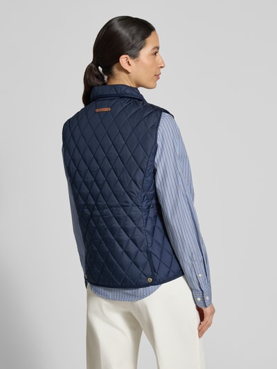Modelka nosi Regular Fit Steppweste mit Umlegekragen od Lauren Ralph Lauren, granatowa, pikowany wzór karo, metaliczne akcenty, naszywka z logo, kieszenie boczne, z rozcięciem z tyłu, widok całej sylwetki od tyłu.