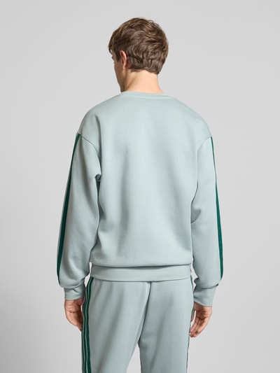 Männermodel trägt Sweatshirt mit Rundhalsausschnitt und Logo von adidas Sportswear im Baumwoll-Mix mit Viskose-Anteil, Regular-Fit, dezentes Hellgrau mit dunklen Akzenten, Rückenlänge 70 cm, Ärmel 64 cm, glatte Textur, Ganzkörperansicht Rückansicht.