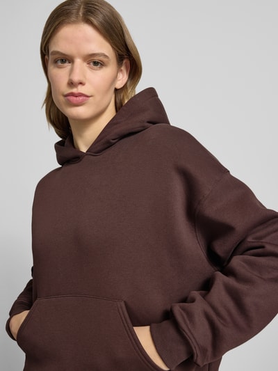 Modelka kobieca nosi Regular Fit Hoodie mit Känguru-Tasche Modell 'Iconic' von Gina Tricot, mieszanka bawełny, krój regular fit, kieszeń kangurka, wykończenia: elastyczne, widok z przodu, zbliżenie na górną część ciała.