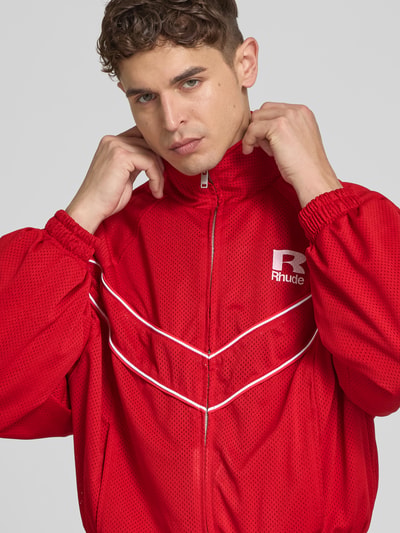 Männermodel trägt Bomberjacke mit Raglanärmeln von RHUDE in Rot mit Stehkragen, Zweiwege-Reißverschluss, Reißverschlusstaschen, Nahaufnahme Oberkörper.