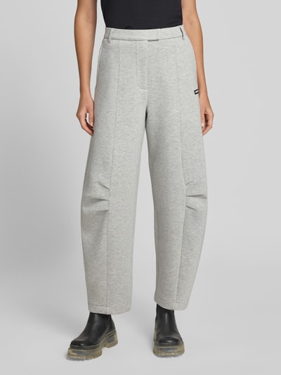 Frauenmodel trägt Hose aus Viskose-Mix von ROTATE in Hellgrau mit Gelegten Falten, Logo-Patch, Relaxed-Fit, Haken-Reißverschluss, Ganzkörperansicht von vorne. Innenbeinlänge bei Größe S 36 cm, Bundweite 80 cm.