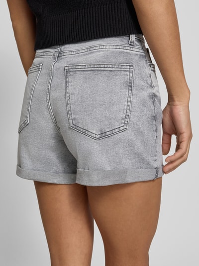 Kobiece model prezentuje szorty jeansowe High Waist Jeansshorts mit Umschlag Modell 'MONI' od Noisy May, mieszanka bawełny i elastanu, wpuszczane kieszenie, brzeg, szerokość w rozmiarze S: 35 cm, długość wewnętrzna nogawki w rozmiarze S: 9 cm, widok całej sylwetki z tyłu