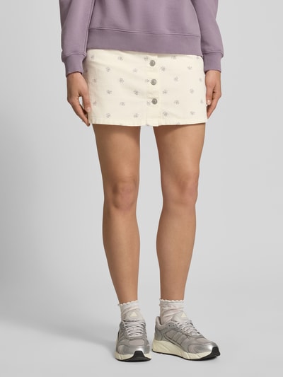Frauenmodel trägt Ausgestellter Mini-Rock aus reiner Baumwolle Modell 'NAOMI' von Only, Florales-Allover-Muster, Twill, Knopfleiste, Eingrifftaschen, Gesäßtaschen, Mini-Länge, Label-Patch, Ganzkörperansicht von vorne.
