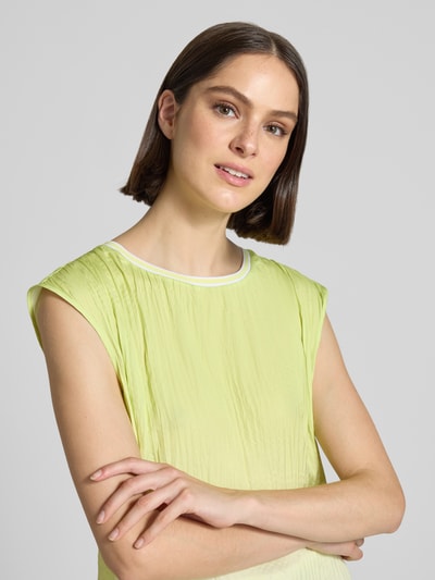 Frauenmodel trägt Bluse mit Strukturmuster und Rundhalsausschnitt von Marc Cain in Hellgelb mit Label-Detail, Nahaufnahme Oberkörper. Rückenlänge 56 cm bei Größe 36, Gerader-Schnitt.