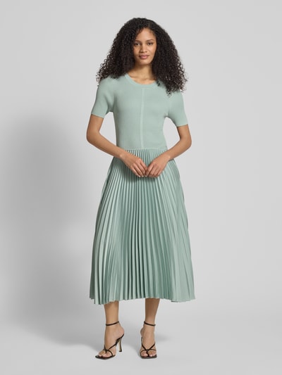 Vrouwenmodel draagt Regular Fit Businesskleid uit verschillende materialen model FADRIDI van BOSS, look: effen, midilengte, ronde hals, plissérok van satijn, korte mouw, materiaalverwerking: ribtricot, satijn, plissé, geheel frontaal.
