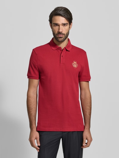 Männermodel trägt Regular Fit Poloshirt aus reiner Baumwolle Modell 'QIANG' von BOSS, Optik: Unifarben, Motiv-Label-Print, Ganzkörperansicht von vorne.