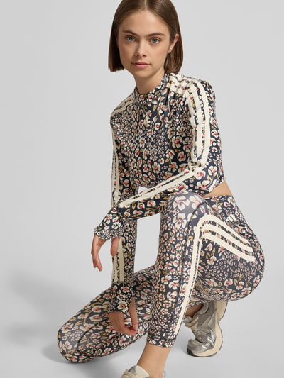 Frauenmodel trägt Slim Fit Sport-Top mit floralem Muster von adidas Sportswear in bunten Farben und schmalen Streifen, Ganzkörperansicht von vorne.