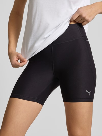 Kobiece modelka nosi Shorts mit elastischem Bund od PUMA, czarna elastyczna mieszanka materiałów, dopasowany krój, nadruk z logo, detal, zbliżenie na biodra.