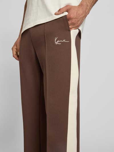 Männermodel trägt Straight Fit Sweatpants mit Logo-Stitching von KARL KANI in Braun mit cremefarbenem Streifen, Elastischer-Material-Mix, Ziernähte, Elastischer Bund, Herren Sweatpants, Nahaufnahme Oberkörper.