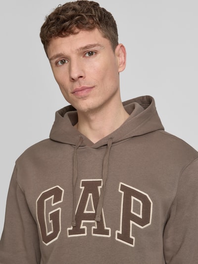 Männermodel trägt Hoodie mit Kängurutasche von GAP in Braun, Baumwoll-Mix, Label-Stitching, lockere Passform, Nahaufnahme Oberkörper.