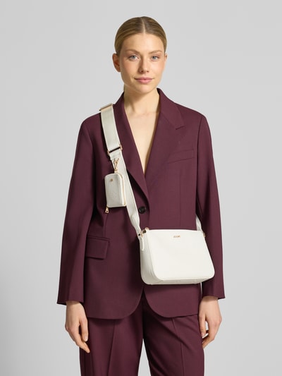 Männermodel trägt Handtasche mit Logo-Muster Modell 'decoro edition jasmina' von JOOP!, cremefarben, strukturierte Oberfläche, abnehmbarer Taschenanhänger, Label-Applikation, Schulterriemen, Szerokość w rozmiarze 24 cm, długość w rozmiarze 16 cm, głębokość w rozmiarze 6 cm, długość paska na ramię w rozmiarze 109 cm, Ganzkörperansicht von vorne.