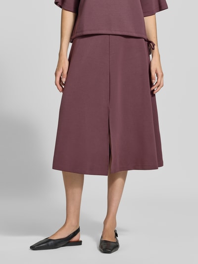 Vrouwenmodel draagt Midirok met elastisch bund van Christian Berg Woman in auberginekleur, elastische materiaalmix met modal, los model, midilengte, bandwijdte maat S 80 cm, detailopname onderlichaam, vooraanzicht.