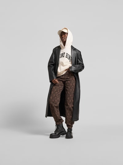 Frauenmodel trägt Oversized Hoodie mit Logo-Print von Anine Bing aus Reiner Baumwolle, Oversized-Fit, Känguru-Tasche, elastische Abschlüsse, Rückenlänge bei Größe S 68 cm, helle und dunkle Farbtöne, Ganzkörperansicht von vorne.