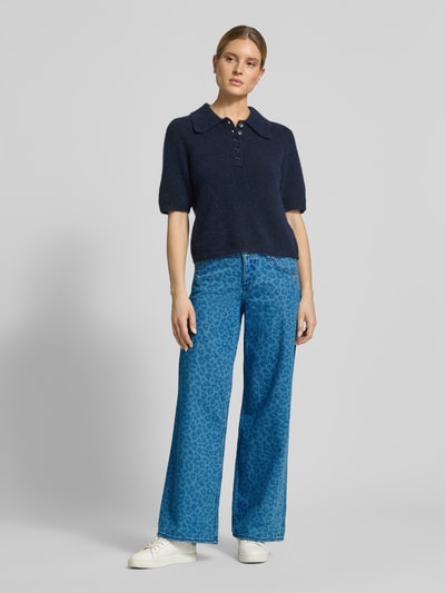 Modelka kobieca nosi Wide Fit Jeans mit Allover-Animal-Print Modell 'Medley' von Mustang z bawełny, 5 kieszeni, zapięcie na guzik i zamek błyskawiczny, szerokość w rozmiarze 27/32: 39 cm, długość wewnętrzna nogawki: 81 cm; wzór w odcieniach niebieskiego, widok całej sylwetki z przodu.
