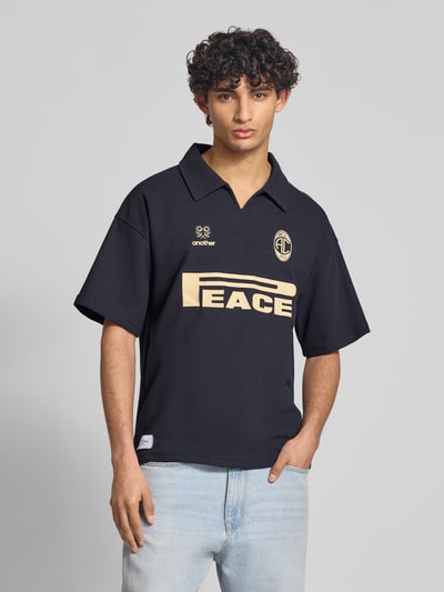Männermodel trägt Regular Fit Poloshirt aus Waffel-Piqué Modell 'Peace' von ANOTHER COTTON LAB in Dunkelblau mit Label-Print, Nahaufnahme Oberkörper.