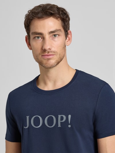 Männermodel trägt T-Shirt mit Logo und Rundhalsausschnitt von JOOP! Collection aus Baumwoll-Elasthan-Mix in Regular-Fit, Nahaufnahme Oberkörper.