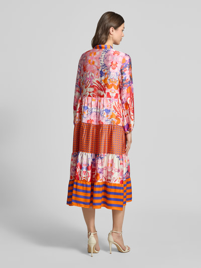 Frauenmodel trägt Midikleid aus Viskose mit V-Ausschnitt Modell 'Wild Flower' von miss goodlife, Allover-Look, A-Linie, Rückenlänge 36 cm, Brustweite 44 cm, Ärmellänge 58 cm, florales Muster in Pink, Orange und Blau, Ganzkörperansicht Rückansicht.