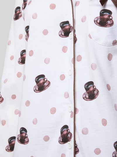 Vrouwenmodel draagt pyjama-Set uit puur katoen Model 'Meine Auszeit' van LOUIS & LOUISA met regular fit, reverskraag, met lange mouwen, borstzak, sierstrik, knoopsluiting, wit met bruine en roze stippen en kopjesprint, detailopname bovenlichaam.