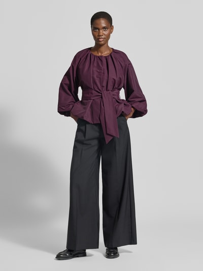 Vrouwenmodel draagt blouse met lange mouwen van Rich & Royal in donkerpaars met strikceintuur, zwarte wijde broek, Ganzkörperansicht von vorne.