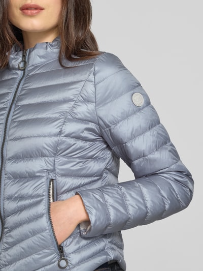 Frauenmodel trägt Steppjacke mit Stehkragen von Gil Bret in Silber, Zweiwege-Reißverschluss, Reißverschlusstaschen, Nahaufnahme Oberkörper. Rückenlänge 56 cm, Schulterbreite 39 cm, Brustweite 47 cm, Ärmellänge 66 cm, Größe 36, Körpernahe Passform.