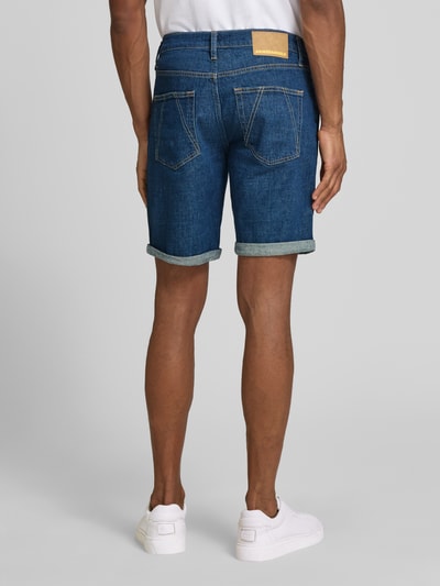 Männermodel trägt Slim Fit Jeansshorts aus Baumwoll-Mix Modell 'NAAILO' von Armedangels, Denim-Optik, Label-Patch, 5-Pocket-Design, Ganzkörperansicht Rückansicht.