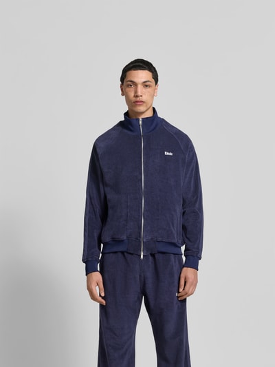 Männermodel trägt Oversized Sweatjacke aus Baumwolle von RHUDE in Dunkelblau mit Frottee, Zweiwege-Reißverschluss, elastische Abschlüsse, Rückenlänge 68 cm, Schulterbreite 48 cm, Ärmellänge 68 cm, Ganzkörperansicht von vorne.