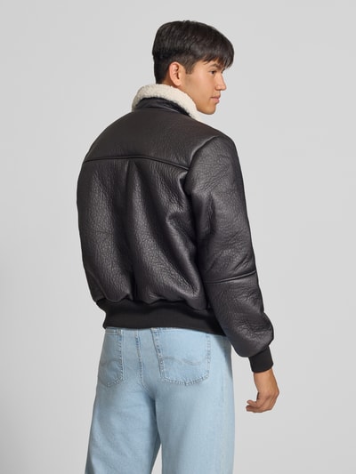 Männermodel trägt Bomberjacke mit Kentkragen und gerippten Abschlüssen von Alpha Industries in Schwarz, Strukturleder-Optik, Rückenansicht. Herren Bomberjacke im Regular Fit mit Teddyfellkragen, Reißverschluss und Druckknopftaschen, Maße bei Größe M: Rückenlänge 66 cm, Schulterbreite 48 cm, Brustweite 55 cm, Ärmellänge 70 cm.