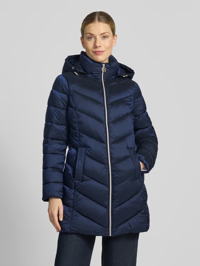 Frauenmodel trägt Steppmantel mit Kapuze und Reißverschlusstaschen von MICHAEL Michael Kors in Dunkelblau, glänzende Oberfläche, Ganzkörperansicht von vorne. Gerader Schnitt, Kapuze mit Tunnelzug, seitliche Reißverschlusstaschen, sichtbare Steppungen, Kontext: Rückenlänge 86 cm, Schulterbreite 43 cm, Brustweite 50 cm, Ärmellänge 62 cm.