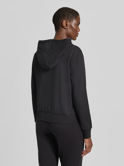 Vrouwenmodel draagt zwarte Sweatjacke met Kapuze Modell 'SOFIA' van GUESS, katoenmix, regular fit, labelstitching, Ganzkörperansicht Rückansicht.