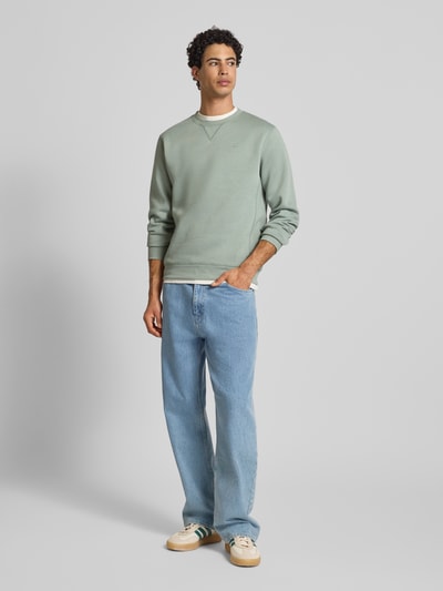 Mężczyzna nosi bluzę z mieszanki bawełny Premium core od G-Star Raw, prosty krój, okrągły dekolt, wyhaftowane logo, elastyczne wykończenia, długość tyłu 66 cm, długość rękawa 67 cm, kolor zielony, faktura gładka, widok całej sylwetki z przodu.
