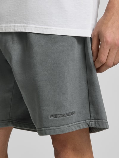 Mężczyzna nosi Shorts mit elastischem Bund und Logo-Stitching von Pegador, szary bawełniany miks, krój loose fit, haftowane logo, detaliczne ujęcie nogawki.