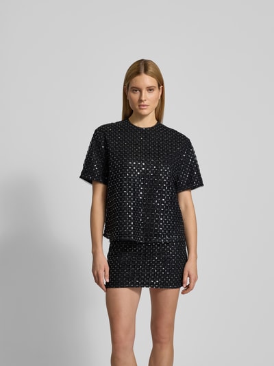 Frauenmodel trägt Oversized T-Shirt mit Ziersteinen von ROTATE, schwarzer Allover-Pailettenbesatz, Rundhalsausschnitt, Kurzärmelig, Ganzkörperansicht von vorne.