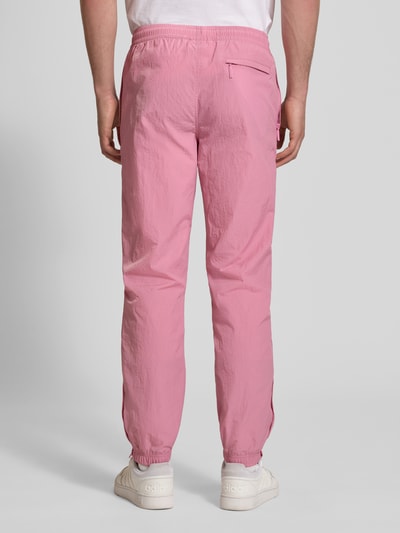 Männermodel trägt Straight Fit Stoffhose mit Logo-Stitching Modell 'Nayla' von SERGIO TACCHINI in Rosa, elastischer Bund mit Tunnelzug, elastische Beinabschlüsse, Innenbeinlänge bei Größe M 77 cm, Ganzkörperansicht Rückansicht.
