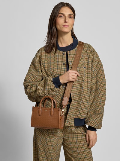 Frauenmodel trägt Henkeltasche mit abnehmbarem Schulterriemen Modell 'SANDY' von BOSS in Braun, Kunstleder mit Geflecht, Ganzkörperansicht von vorne.