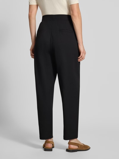 Frauenmodel trägt Relaxed Fit Anzughose mit Bundfalten Modell 'SC-SIHAM 103' von Soyaconcept in Schwarz, glatte Oberfläche, Ganzkörperansicht Rückansicht, Damen Anzughose.
