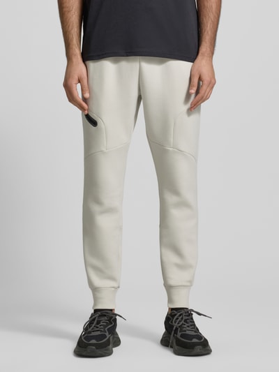 Männermodel trägt Regular Fit Sweatpants mit Logo-Print Modell 'Unstoppable' von Under Armour, Elastischer-Material-Mix mit Baumwoll-Anteil, Herren, Beintasche mit Reißverschluss, Elastischer Bund, Elastische Beinabschlüsse, Innenbeinlänge 73 cm, helle Farbe, glatte Struktur, Ganzkörperansicht von vorne.
