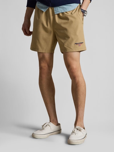 Männermodel trägt Badeshorts mit Label Stitching van Polo Ralph Lauren in effen beige met labelapplicatie, elastische tailleband, zijzakken, achterzak; Ganzkörperansicht von vorne.