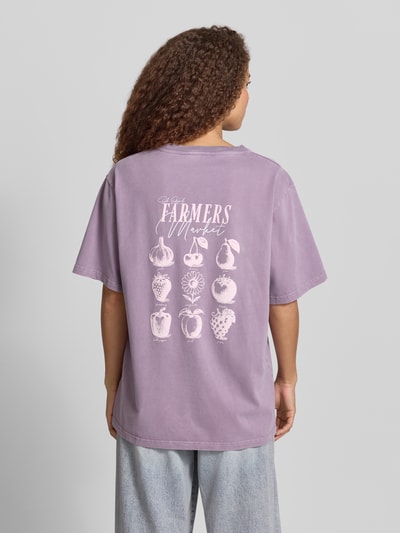 Frauenmodel trägt Damen T-Shirt von OH APRIL in Flieder mit Oversized-Schnitt, Rundhalsausschnitt, Label-Stitching, Reine Baumwolle, Rückansicht, Rückenlänge bei Größe S: 72 cm, Modell 'Farmers Market'.