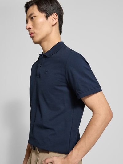 Męski model nosi Regular Fit Poloshirt aus reiner Baumwolle von Tom Tailor, gładki granat, krój regular fit, logo, piqué, bawełna, krótkie rękawy, widok z boku na górną część ciała.